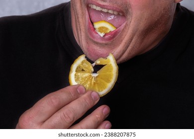 An unrecognizable man eats a sour lemon.