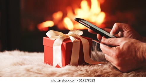 Unrecognizable Man Hands holding Credit Card and Using SmartPhone by the Burning Fireplace and Festive Presents - Close Up. Man with phone key-green screen by cozy fireside.