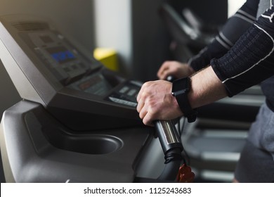Unrecognizable man hands on elliptical trainer handrails in sport club. Cardio workout background, running on treadmill. Healthy lifestyle, guy training in gym, side view, copy space