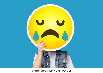 Unrecognizable Man Hiding His Face Behind Crying Sad Emoticon Emoji Over Blue Background, Creative Collage With Copy Space