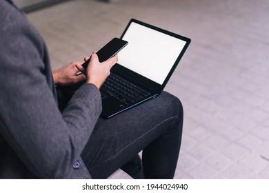 Unrecognizable Man With His Cell Phone While Sitting On A Bench With His Laptop With White Screen.