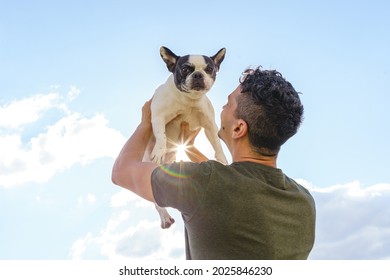 Unrecognizable man holding up a bulldog. Horizontal view of man with pet outdoors. Lifestyle with animals - Powered by Shutterstock