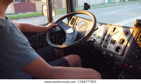 Unrecognizable man holding his hand on steering
wheel and driving truck at urban road. Arm of trucker at wheel of
car. Lorry driver rides to destination. View from inside car cab.
Slow motion.