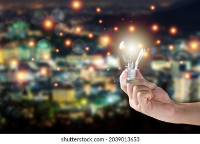 Unrecognizable Man Holding The Illuminated Vintage Tungsten Lightbulb On Night City Blurred Background With Copyspace. Creativity And Idea Concept. 