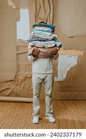 Unrecognizable man holding stack of clothes standing over craft paper cardboard background. Recycling upcycling concept.