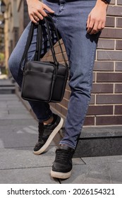 Unrecognizable Man Holding Two Messenger Bags In His Hands Leaning At Brick Wall