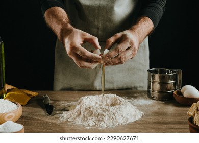 Unrecognizable man kneading dough on wooden background against dark wall. Close-up of male hands cutting egg. Stage 2 of preparation homemade noodles. Selective focus. - Powered by Shutterstock