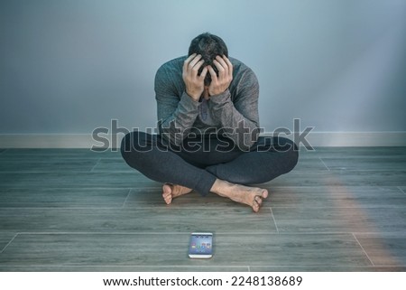 Unrecognizable man with problems covering face sitting on the floor behind of his mobile