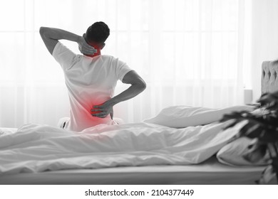 Unrecognizable Man Rubbing Painful Back And Neck After Waking Up In The Morning, Male Sitting In Bed And Touching Red Sore Areas, Suffering Backache And Spine Problems At Home, Rear View, BW Shot