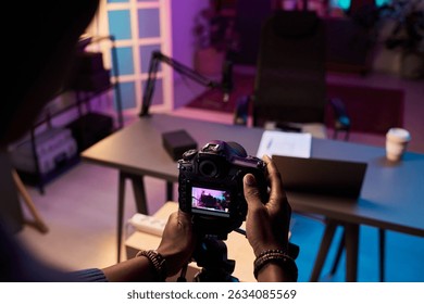 Unrecognizable man setting up camera on tripod for filming content. in neon lit studio environment with modern decor visible in background