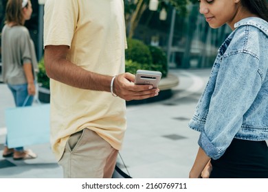 Unrecognizable Man Showing Mobile Phone To His Female Friend Outdoors. 
Close Up Photo Of Man Hand Using Smartphone While He Standing At City Street With A Cute Teenager Girl.