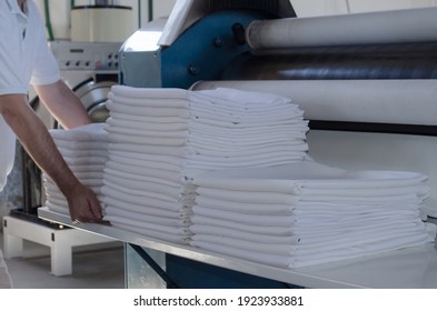 Unrecognizable Man Stacking Freshly Ironed Sheets Or Fabrics In An Industrial Laundry. Cleaning And Ironing Service For Hotels, Clinics And Companies.