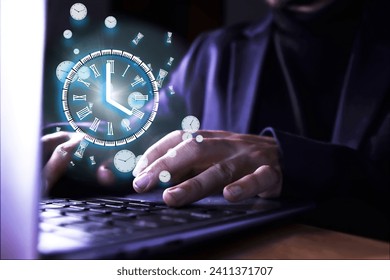 Unrecognizable man using the computer with a clock indicating the time of use of the pc. Abusive use of the computer. Control of the time, too many hours of work in front of a screen. Remote work.