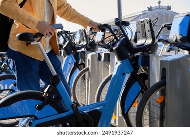 Unrecognizable man using her smartphone to rent a bicycle from the bike rental station to ride around the city - Powered by Shutterstock