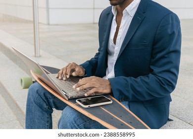 Unrecognizable man using laptop while sitting on skateboard during daylight on street