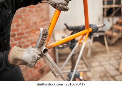 Unrecognizable man using a wire brush over a bicycle frame after passing a blowtorch over it to remove the paint, as part of his bike renovation work.