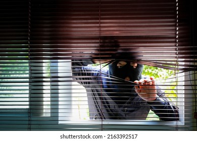 Unrecognizable Man Wearing Balaclava Face Mask Looking Through Venetian Blinds. Keep Your Home Secure During Your Summer Holiday Concept.