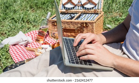 Unrecognizable Man In White Pants Outside Having Picnic And Using Laptop, Working Outdoors. Summer Leisure And Fun