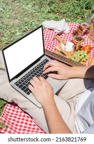 Unrecognizable Man In White Pants Outside Having Picnic And Using Laptop, Working Outdoors. Summer Leisure And Fun