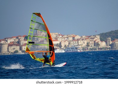 Unrecognizable man windsurfs past the ancient old town of Korcula, Croatia on a sunny summer day. Fit male tourist on active vacation kitesurfs along the coastline of the spectacular Korcula island. - Powered by Shutterstock