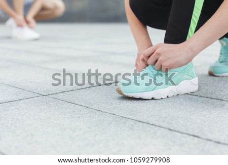 Unrecognizable man and woman tying shoelaces on sneakers before running, getting ready for jogging in city centre, closeup, copy space, crop, selective focus on woman feet