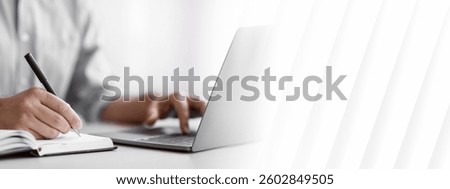 Unrecognizable Man Writing In Notepad And Using Laptop In Office, Taking Notes At Workplace, Using Computer, Noting Information From Internet, Cropped Image With Selective Focus On Hand, Closeup