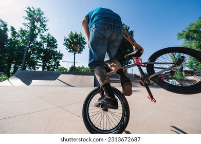 An unrecognizable mature professional freestyle bmx rider is performing tricks and stunts in a skate park. A middle-aged tattooed extreme man is practicing for the X-games tournament. - Powered by Shutterstock