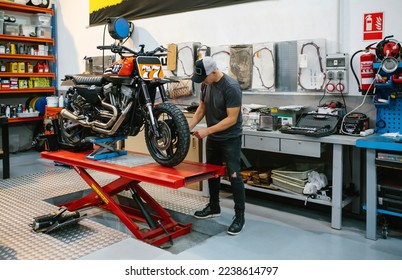 Unrecognizable mechanic man checking engine of custom motorcycle over platform on factory - Powered by Shutterstock