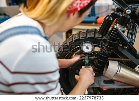 Unrecognizable mechanic woman with manometer checking tire air pressure of motorcycle on factory