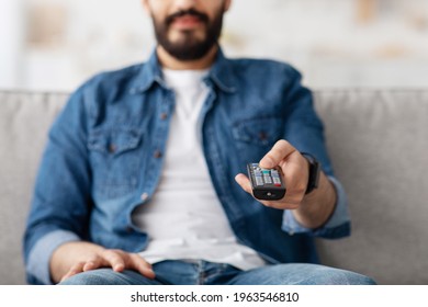 Unrecognizable Middle Eastern Guy Watching TV At Home And Switching Channels With Remote Controller, Closeup, Selective Focus. Arab Man Relaxing On Couch And Enjoying Domestic Weekend