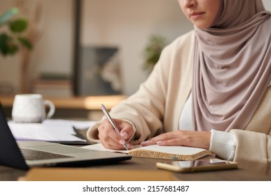 Unrecognizable Middle Eastern Woman Wearing Headscarf Working At Office Table Writing Something In Her Notebook