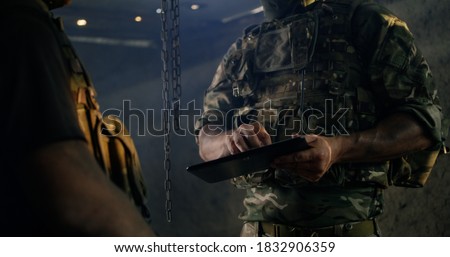 Unrecognizable military officers using tablet and examining battle plans in dark room during war