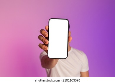 Unrecognizable Millennial Guy Holding Modern Cellphone With Empty White Screen In Front Of His Face In Neon Light, Offering Mockup For Mobile App, Ad Or Website Design. Online Advertisement Concept