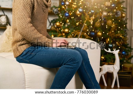 unrecognizable model using laptop at home during christmas. Buying online new year gifts. Christmas tree blur on background. Cozy apartment decorated lights and deer