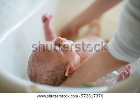 Unrecognizable mother bathing her son in white small plastic bat