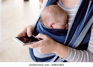 Unrecognizable mother with her son in sling, holding smartphone - Powered by Shutterstock