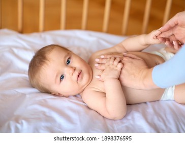 Unrecognizable Mother Massaging Her Cute Little Baby Body. Closeup Of Adorable Kid Toddler Looking At Camera While Playing With Mom Hands After Waking Up, Laying In Wooden Baby Bed