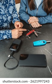 Unrecognizable mother pointing at multi tool knife while explaining 72 hours emergency kit to teenage daughter with power bank, lighter and mobile. Alert, foresight and self sufficiency strategy.