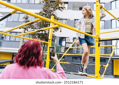 Unrecognizable mother shooting with smart phone preteen daughter l sitting on monkey bars at playground outdoor. Kid, adventure and fun on jungle gym playground, balance or energy for physical growth. - Powered by Shutterstock