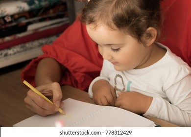 Unrecognizable mother teaching her small girl to write while spending time together.