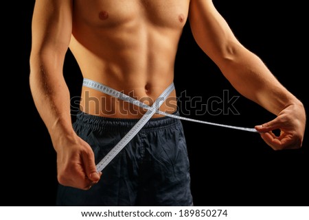 Unrecognizable muscular man is measuring waist with tape