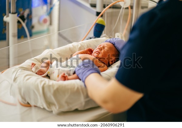 Unrecognizable nurse in blue\
gloves takes action and care for premature baby, selective focus on\
baby eye Newborn is placed in the incubator. Neonatal intensive\
care unit