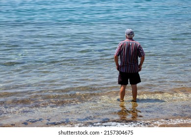 Unrecognizable Old Man Standing On The Beach And Looking At The Sea. Sunny Summer Day