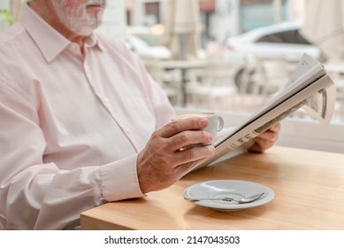 An Unrecognizable Older Man Reading A Daily Newspaper While Drinks His Coffee Sitting At The Table In A Coffee Shop