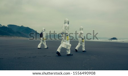 Unrecognizable people with bacteriological protection suits walking on the sand of the beach