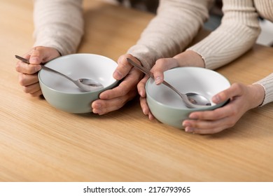 Unrecognizable People Husband And Wife Sitting At Kitchen Table With Spoons In Empty Plates, Hungry Family Has Nothning To Eat, Suffering From Hunger While Crisis During Pandemic, Cropped