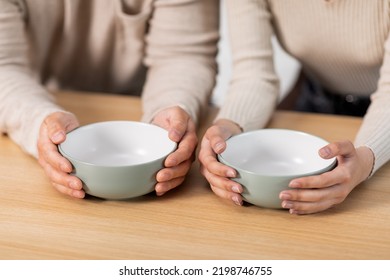 Unrecognizable People Husband And Wife Sitting At Kitchen Table With Empty Bowls, Hungry Family Has Nothning To Eat, Suffering From Hunger While Crisis During Coronavirus Pandemic, Cropped