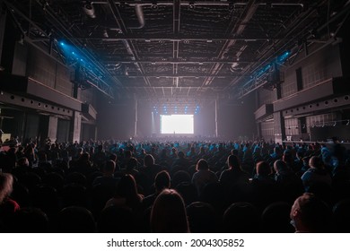 Unrecognizable people sitting on chairs in front of stage with blank screen during business conference in dark hall - Shutterstock ID 2004305852