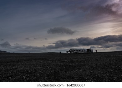 Unrecognizable people surrounding famous DC-3 plane wreckage on a black sand beach, in Iceland