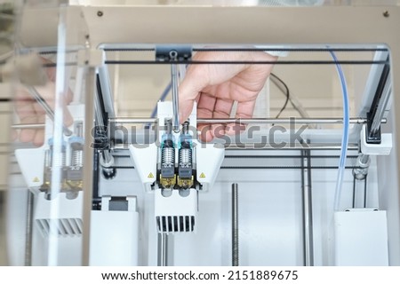 Unrecognizable person changing plastic 3D printer nozzles or extruders.